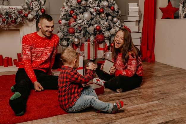 Familia feliz con el niño celebrando el año nuevo y la Navidad en el árbol de Navidad decorado y guirnaldas