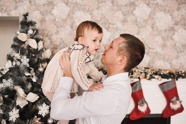 Familia feliz con el niño celebrando el año nuevo y la Navidad en el árbol de Navidad decorado y guirnaldas