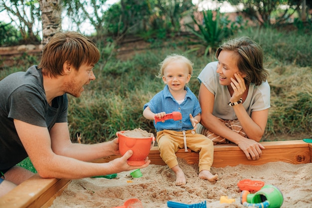 Familia feliz con niño pequeño jugando en el arenero