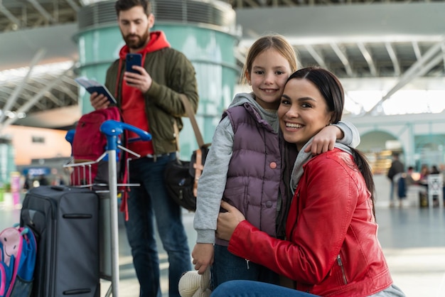 Foto familia feliz con un niño pequeño viajando en avión. madre abrazando a su hija sentada en el aeropuerto. padre de pie en el fondo. concepto de viaje