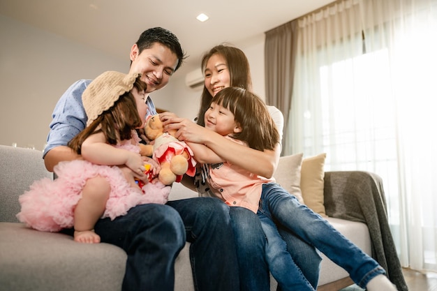 Familia feliz Los niños están sentados en el regazo de los padres en el sofá de la sala de estar Los niños se divierten jugando con el oso de peluche juntos Actividad de fin de semana concepto de estilo de vida familiar feliz