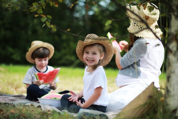 Familia feliz con niños haciendo un picnic en el parque, padres con niños sentados en el césped del jardín y comiendo sandía al aire libre