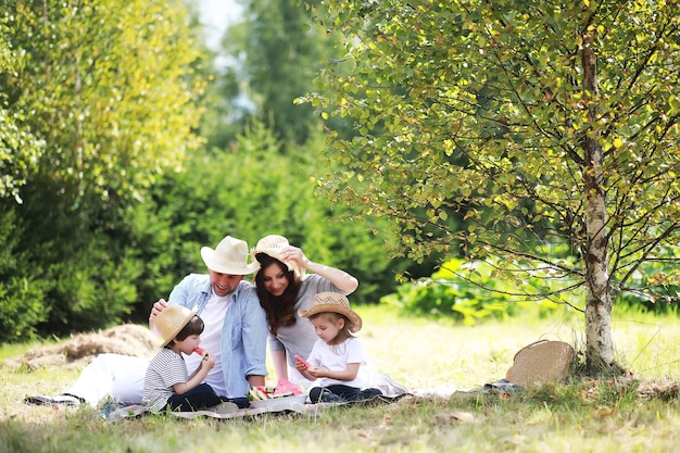 Familia feliz con niños haciendo un picnic en el parque, padres con niños sentados en el césped del jardín y comiendo sandía al aire libre