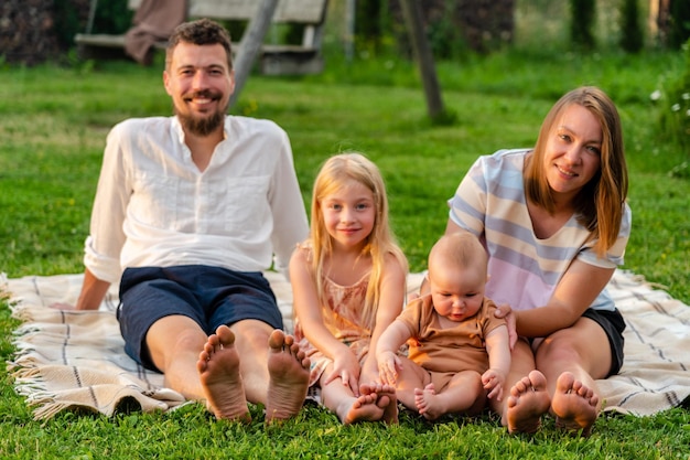 Familia feliz y niños pequeños en una manta en la hierba en verano