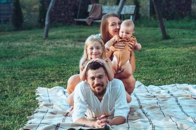 Familia feliz y niños pequeños en una manta en la hierba en verano
