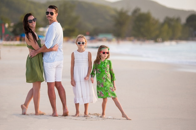 Familia feliz con niños a pie en la playa al atardecer