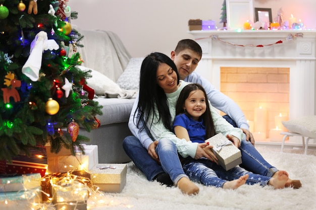 Família feliz no chão com presentes na sala decorada de Natal