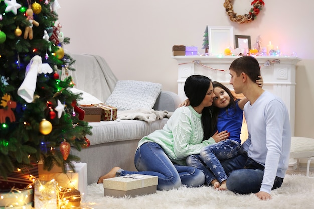 Família feliz no chão com presentes na sala decorada de Natal