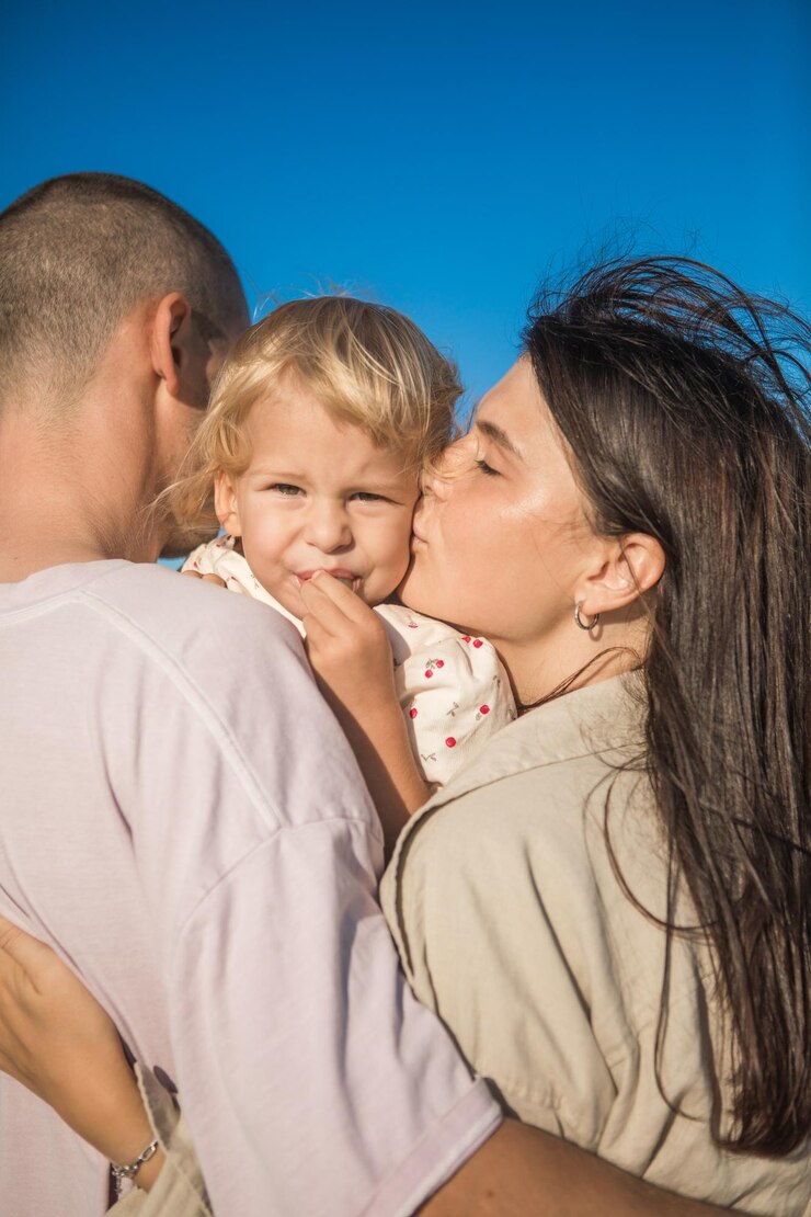 Família feliz no oceano Os pais beijam a filha