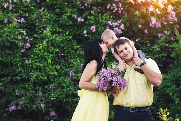 Família feliz no parque com floração lilás. mãe, pai e filho feliz caminham ao pôr do sol. conceito de família feliz. filho se senta sobre os ombros do papa.