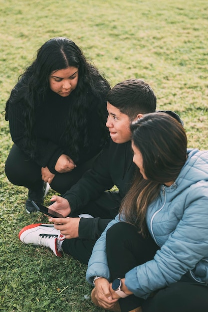 Família feliz no parque sentada a ver e a partilhar smartphones.