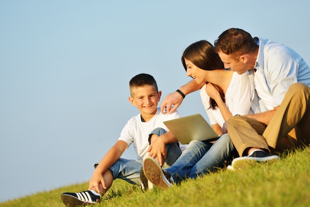 Família feliz no prado de verão bonito tendo tempo feliz com laptop