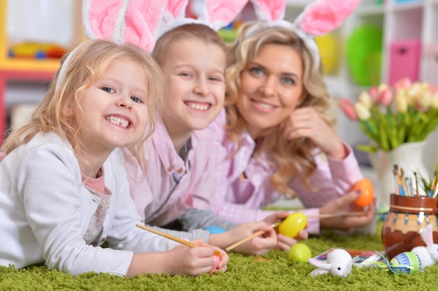 Familia feliz con orejas de conejo preparándose para Pascua y huevos de colores.