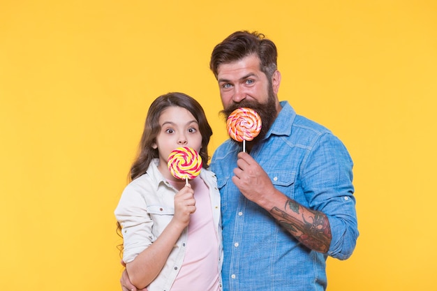 Familia feliz padre e hija comen piruleta fondo amarillo concepto de caramelo casero