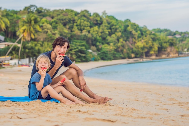 Familia feliz Padre e hijo comiendo una sandía en la playa. Los niños comen alimentos saludables.