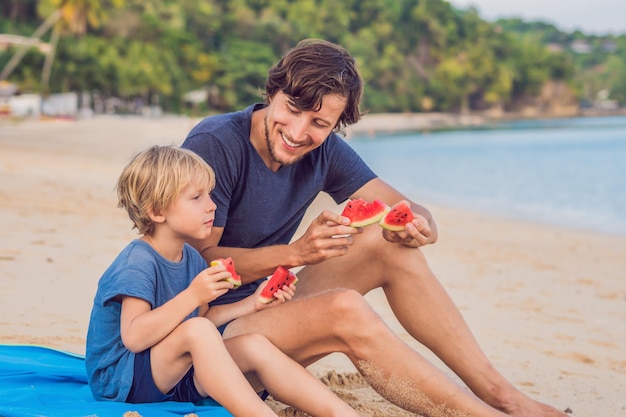 Familia feliz Padre e hijo comiendo una sandía en la playa. Los niños comen alimentos saludables.