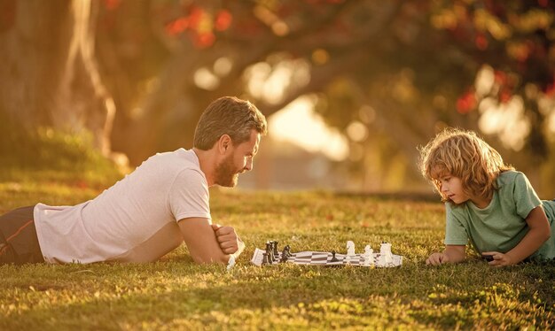 Familia feliz de padre e hijo jugando al ajedrez en la hierba verde en la concentración al aire libre del parque