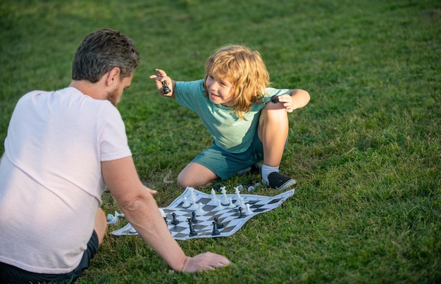 Familia feliz de padre e hijo jugando al ajedrez en la hierba verde en el juego de ajedrez al aire libre del parque