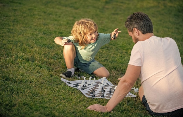 Familia feliz de padre e hijo jugando al ajedrez en la hierba verde en el juego de ajedrez al aire libre del parque