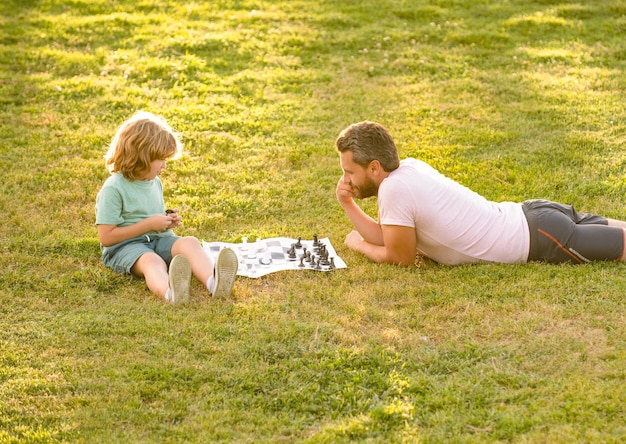 familia feliz de padre e hijo jugando al ajedrez en la hierba verde en el parque al aire libre, ajedrez.