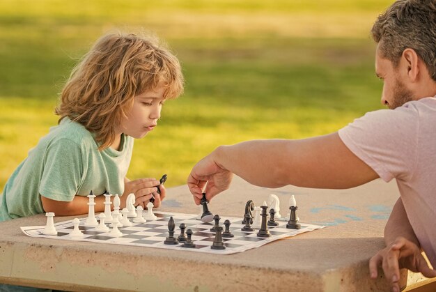 Familia feliz de padre e hijo jugando al ajedrez en la mesa en el torneo de ajedrez al aire libre del parque