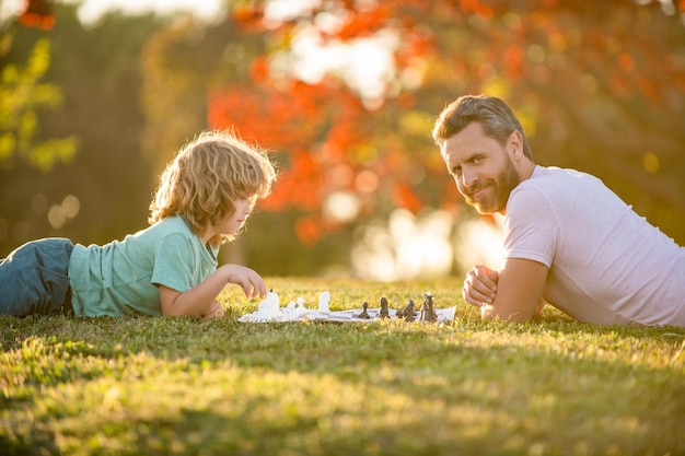 Foto familia feliz de padre hombre e hijo niño jugando al ajedrez en la hierba verde en el parque deporte lógico al aire libre