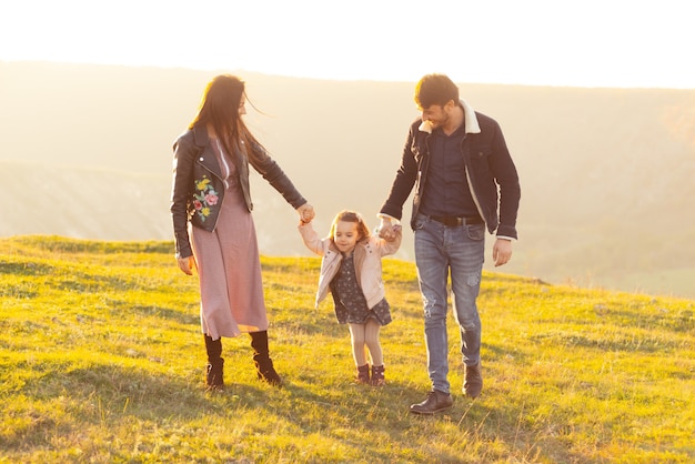 Familia feliz, padre madre e hija del niño en la naturaleza en la puesta del sol