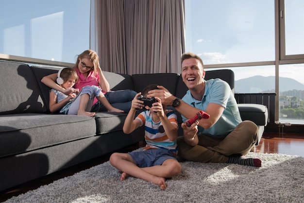 Familia feliz. Padre, madre e hijos jugando videojuegos Padre e hijo jugando videojuegos juntos en el suelo