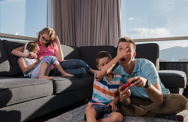 Familia feliz. Padre, madre e hijos jugando videojuegos Padre e hijo jugando videojuegos juntos en el suelo