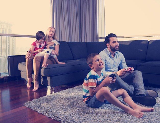 Familia feliz. Padre, madre e hijos jugando videojuegos Padre e hijo jugando videojuegos juntos en el suelo