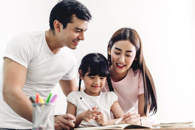 Familia feliz padre y madre con hija aprendiendo y escribiendo en el cuaderno con lápiz haciendo la tarea en casa. Concepto de educación