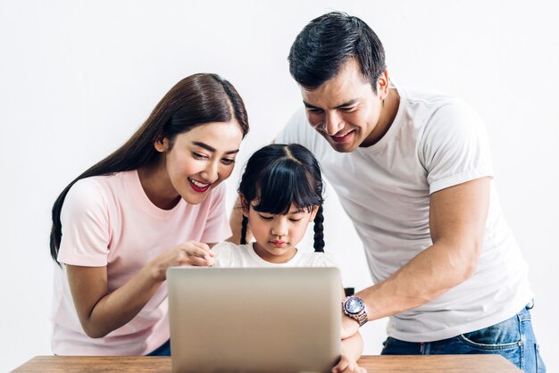 Familia feliz padre y madre con hija sentada y mirando la computadora portátil juntos en la sala de estar en casa