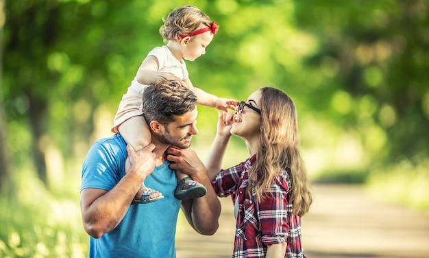 Família feliz, pai, mãe e filha estão brincando no parque e curtindo um dia ensolarado de verão.