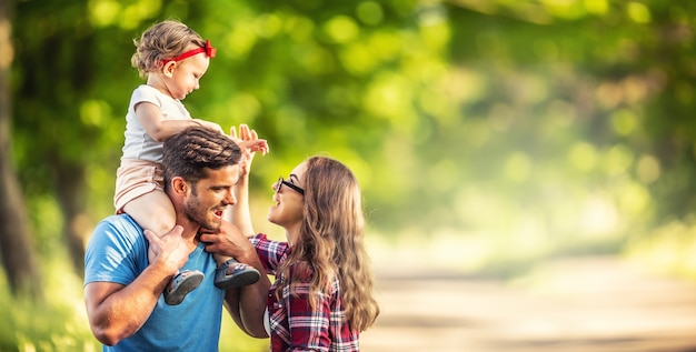 Família feliz, pai, mãe e filha estão brincando no parque e curtindo um dia ensolarado de verão.