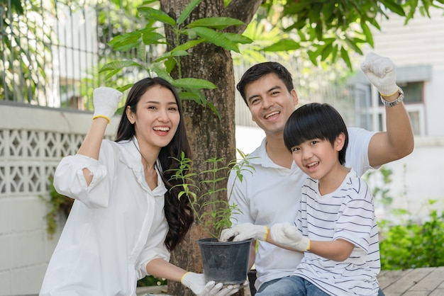 Família feliz, pai, mãe e filho ajudam juntos a plantar uma árvore no jardim em casa atividade nas férias