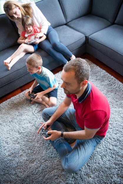 Família feliz. Pai, mãe e filhos jogando videogame Pai e filho jogando videogame juntos no chão