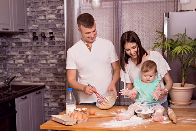 Familia feliz, papá, mamá e hija juegan y cocinan en la cocina, amasan la masa y hornean galletas