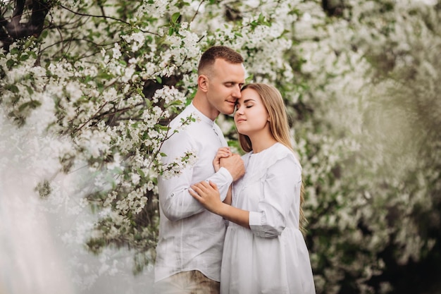 Familia feliz pareja enamorada en un huerto de manzanos en flor de primavera Familia feliz disfruta mientras camina en el jardín El hombre sostiene la mano de la mujer Relaciones familiares