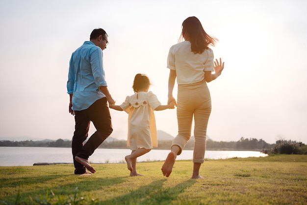 Familia feliz en el parque luz del atardecer familia en el fin de semana corriendo juntos en el prado con el río Los padres toman las manos del niño