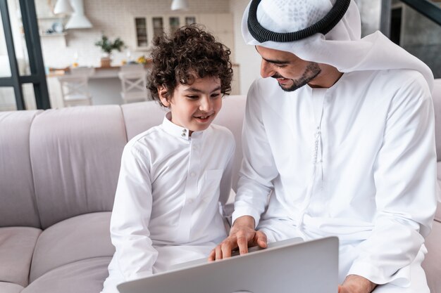Familia feliz pasar tiempo juntos. Padre árabe y su hijo estudiando juntos en la computadora