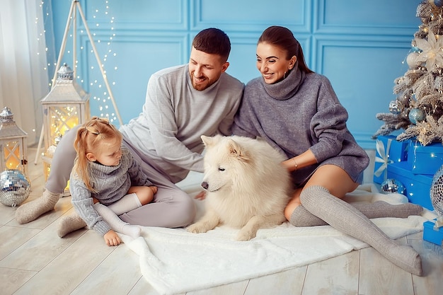 Familia feliz, pequeña hija, mamá y papá pasan tiempo con mascotas cerca del árbol de Navidad en la sala de estar