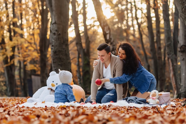 Familia feliz con el pequeño niño lindo en parque en la hoja amarilla con la calabaza grande en otoño