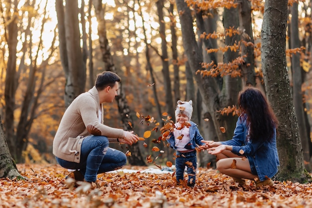 Familia feliz con el pequeño niño lindo en parque en la hoja amarilla con la calabaza grande en otoño