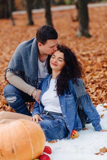 Familia feliz con el pequeño niño lindo en parque en la hoja amarilla con la calabaza grande en otoño