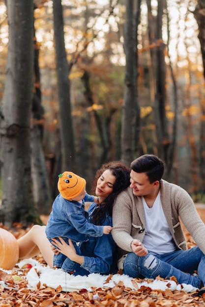 Familia feliz con el pequeño niño lindo en parque en la hoja amarilla con la calabaza grande en otoño