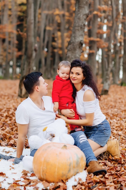 Familia feliz con el pequeño niño lindo en parque en la hoja amarilla con la calabaza grande en otoño