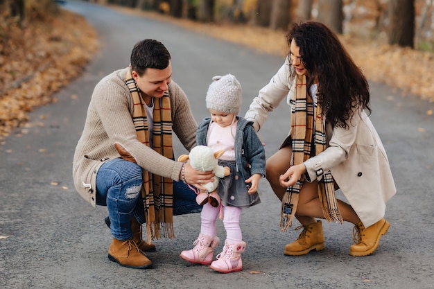 Familia feliz con el pequeño paseo del bebé en el camino del parque con los árboles amarillos en el otoño