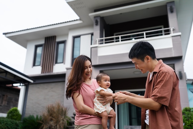 Familia feliz de pie fuera de su casa, marido y mujer y bebé