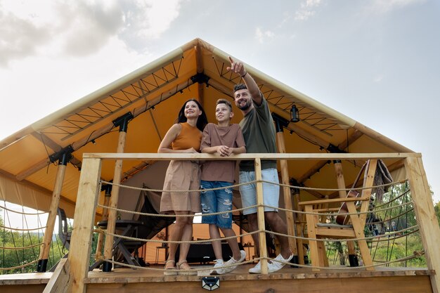 Familia feliz de pie junto a la casa de glamping en entorno natural