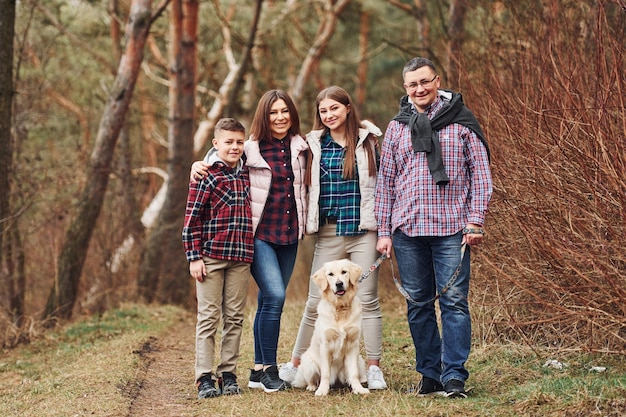 Familia feliz de pie junto a su perro al aire libre en el bosque